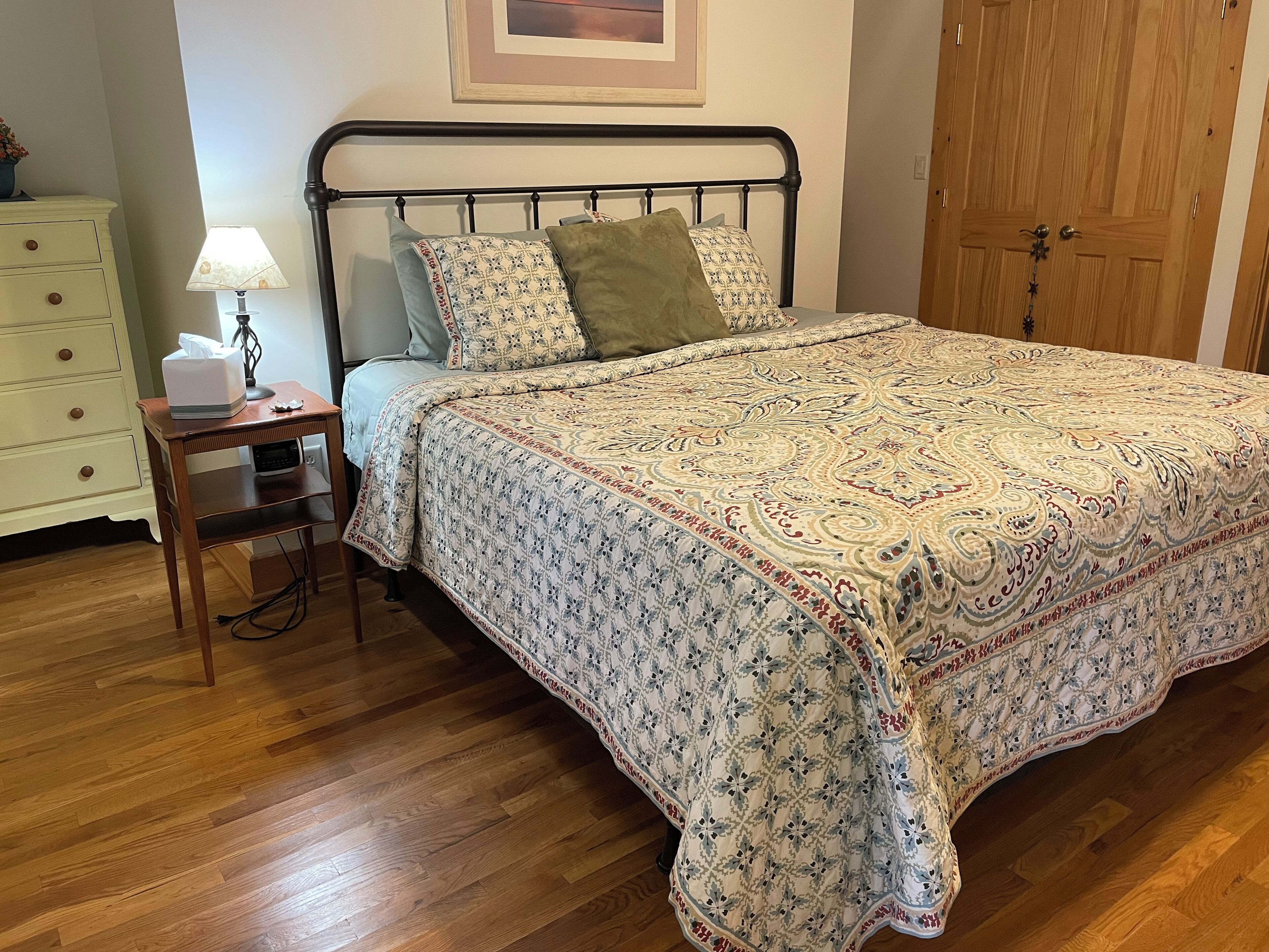 A neatly made bed with a patterned bedspread, a bedside table with a lamp, and a dresser with drawers.