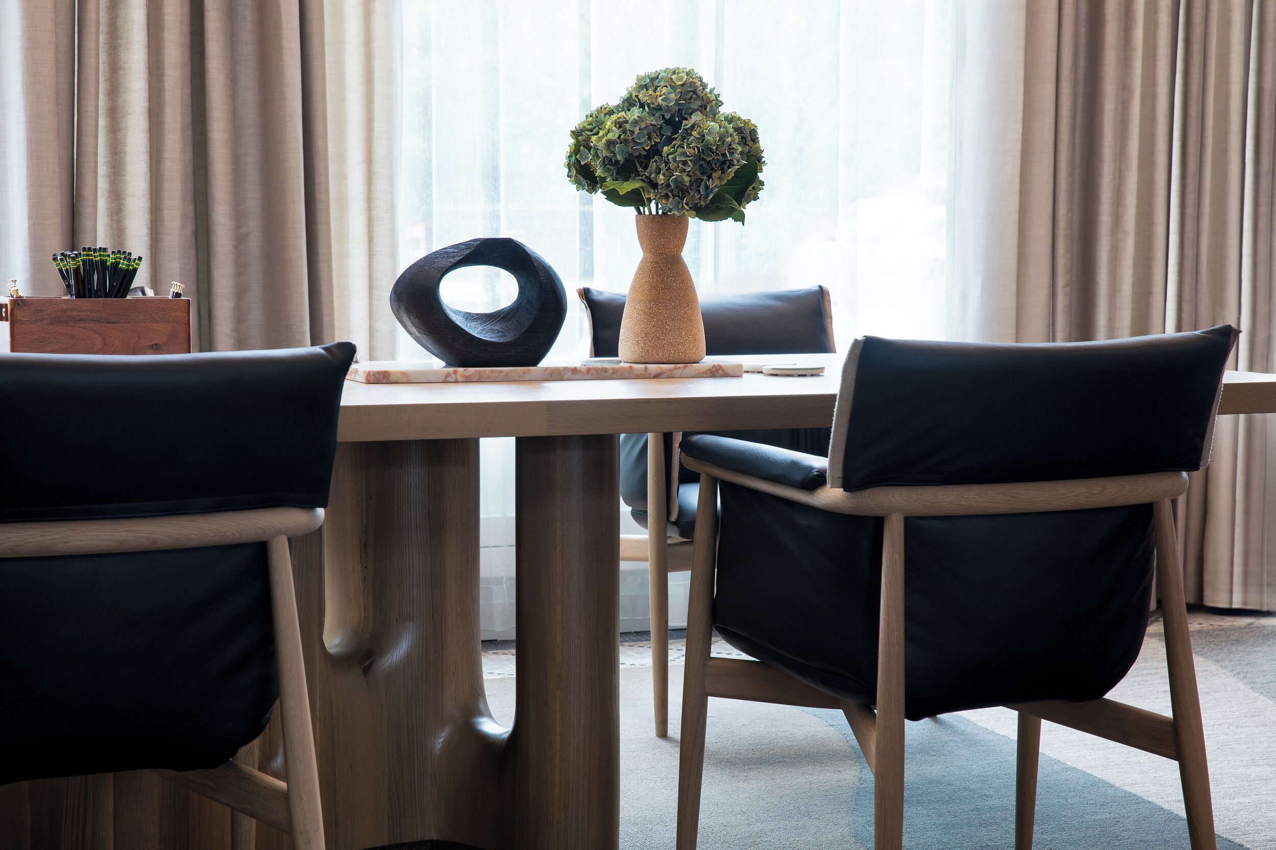 Un espace repas moderne avec une table en bois, des chaises noires, un vase avec des plantes vertes et un anneau décoratif sur la table.