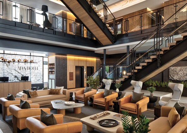 A spacious lobby with a high ceiling, multiple seating areas, a staircase, and a reception desk with a map backdrop.