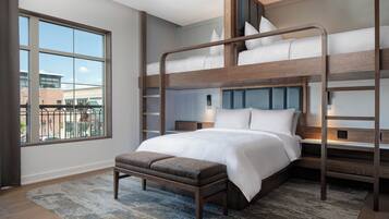 A bunk bed room with a large window, a bench, and a patterned rug.