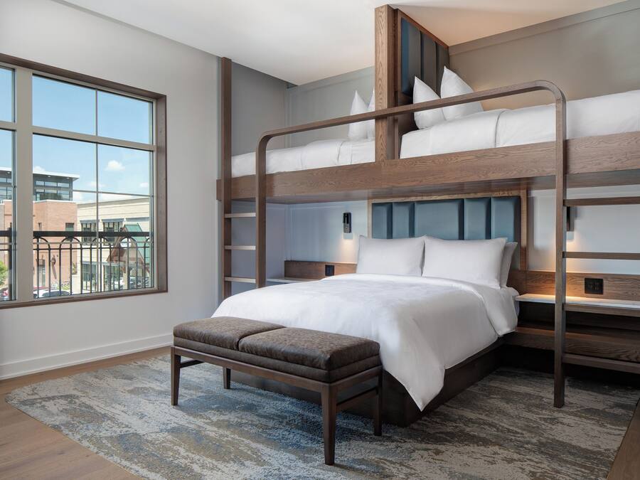 A bunk bed room with a large window, a bench, and a patterned rug.