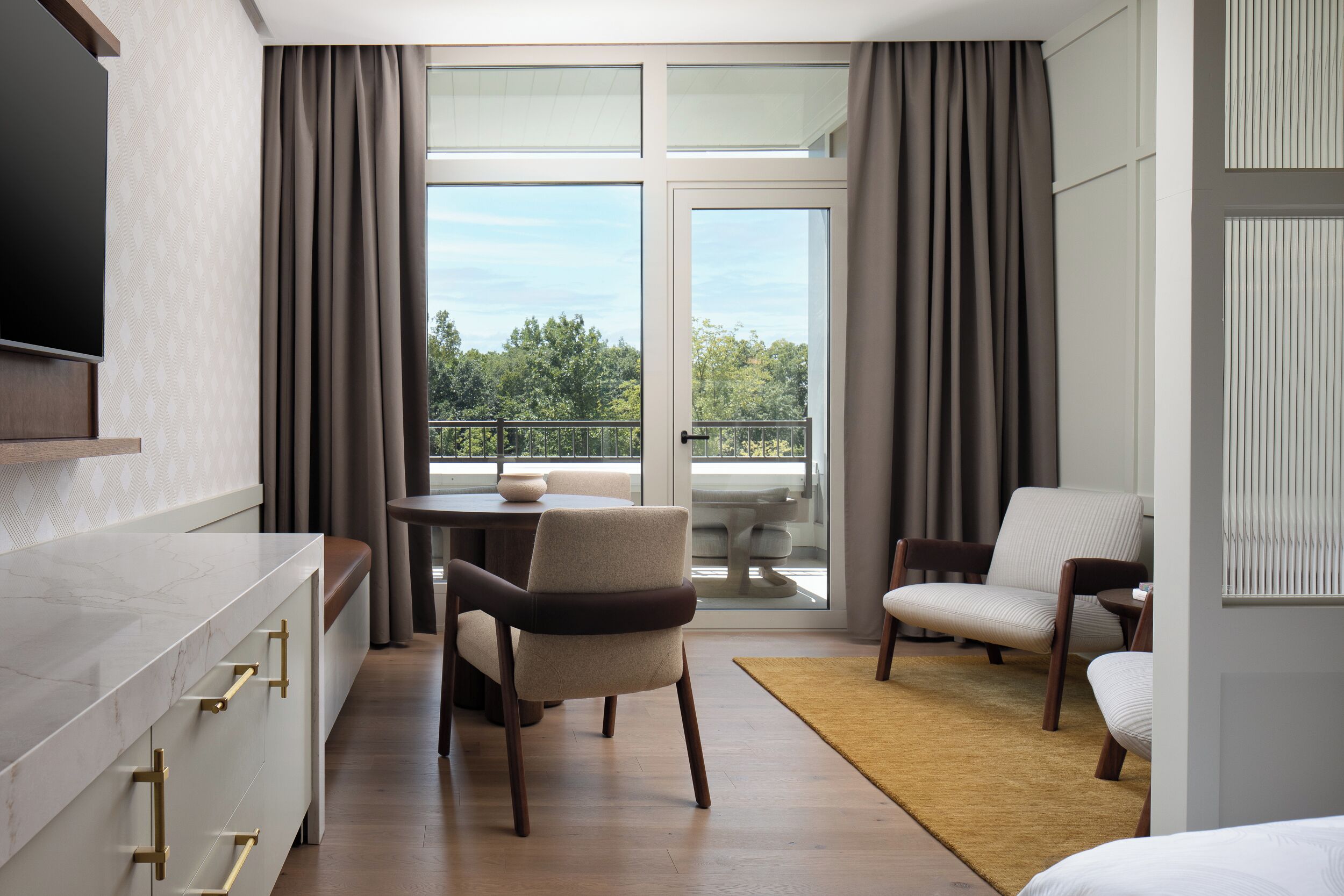 A modern hotel room with a large window, a dining area, and a sofa.