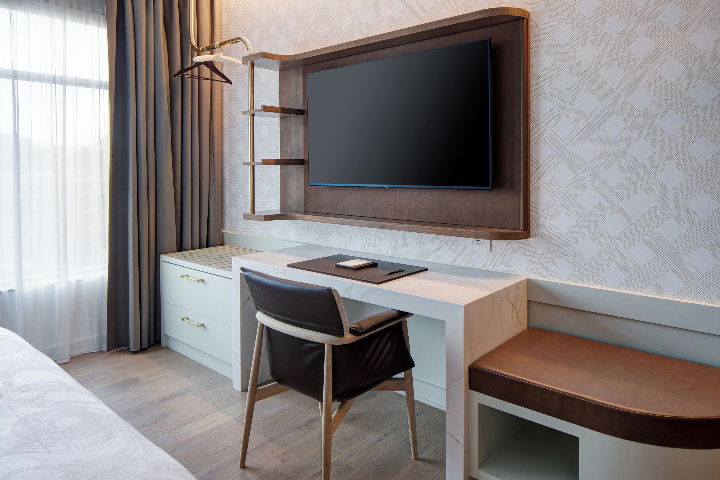 A modern hotel room with a wooden desk, a flat-screen TV, a chair, and a bed.