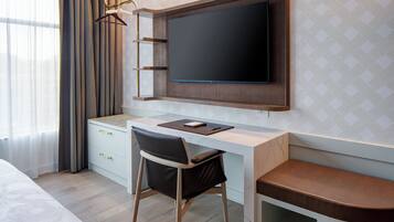 A modern hotel room with a wooden desk, a flat-screen TV, a chair, and a bed.