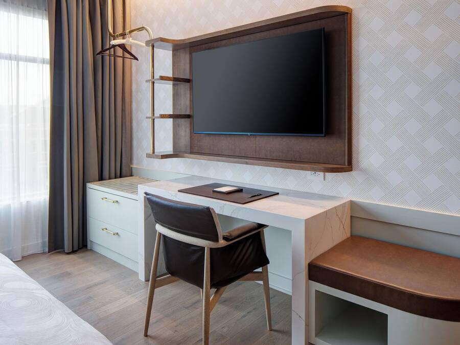 A modern hotel room with a wooden desk, a flat-screen TV, a chair, and a bed.