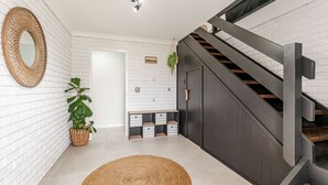 A modern interior with a staircase, white brick walls, a mirror, a welcome sign, and storage units. - Sunset Waters - Waterfront with Pool - Holiday Yamba (Yamba)