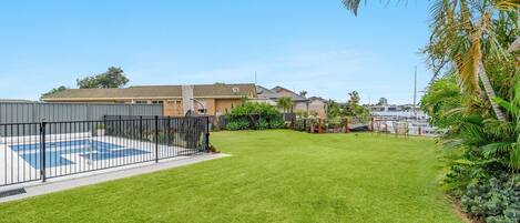 A residential backyard with a swimming pool, a well-maintained lawn, and a view of a marina with boats.