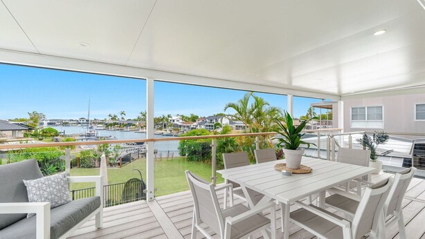 A spacious balcony with a white table and chairs, overlooking a marina and lush greenery. - Sunset Waters - Waterfront with Pool - Holiday Yamba (Yamba)
