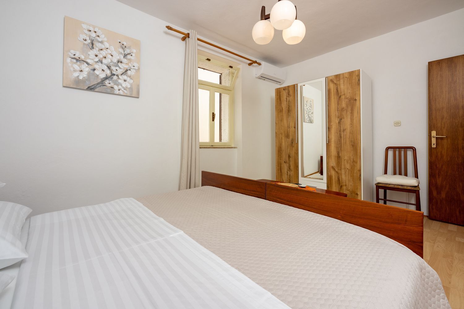 A bedroom with a large bed, a wooden wardrobe, a chair, and a painting on the wall.