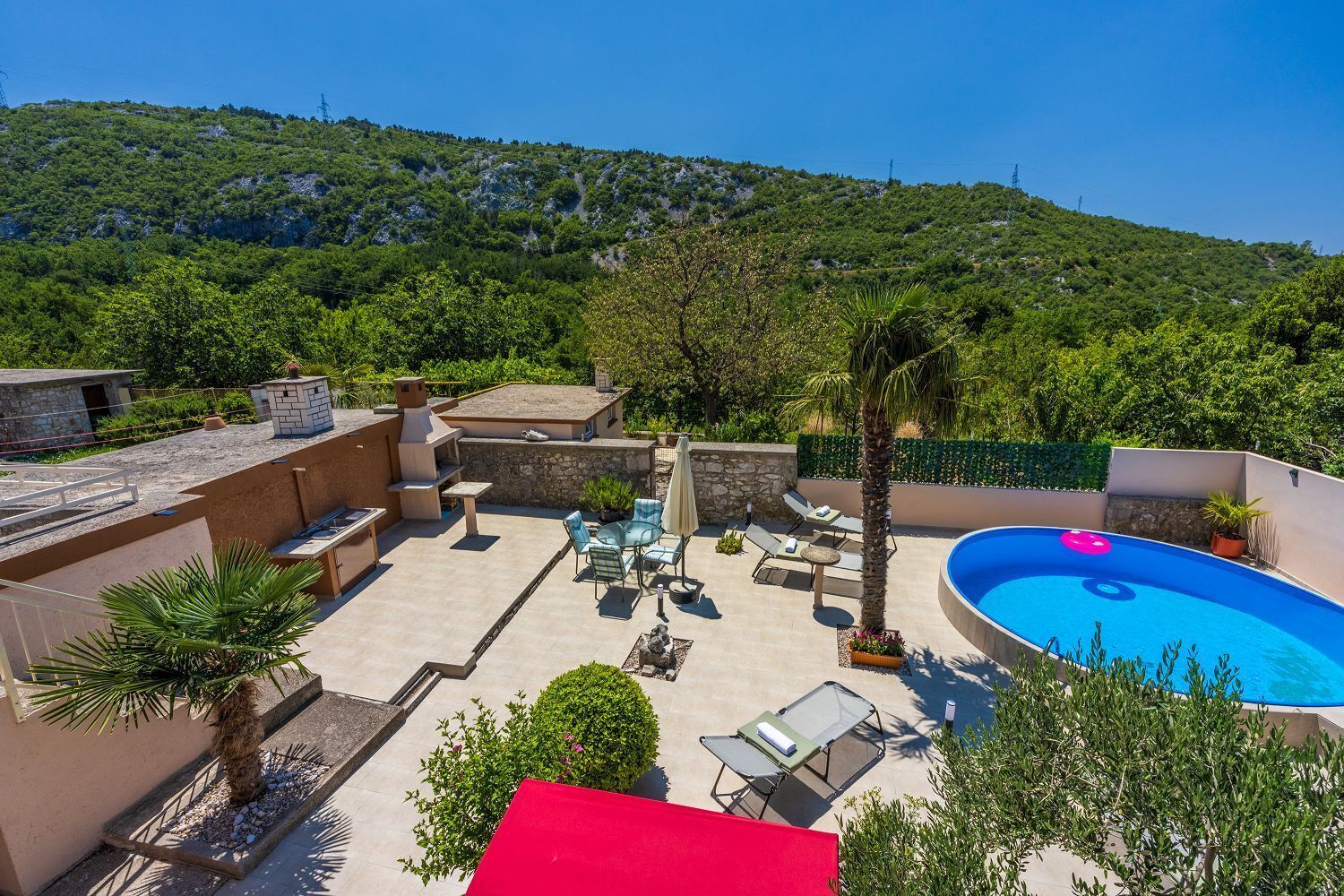 A rooftop patio with a swimming pool, outdoor furniture, and a stone barbecue area.