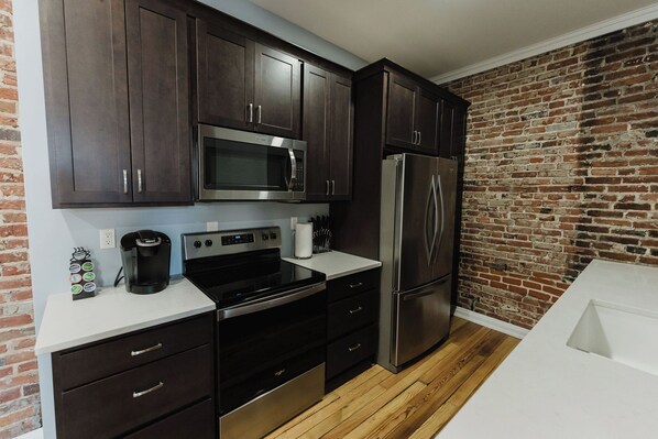 A modern kitchen with dark wooden cabinets, stainless steel appliances, and a brick wall. - Walk to Arch, Stadium & Dome! 2BR/2BA Downtown Gem ready for you and your family (St. Louis)