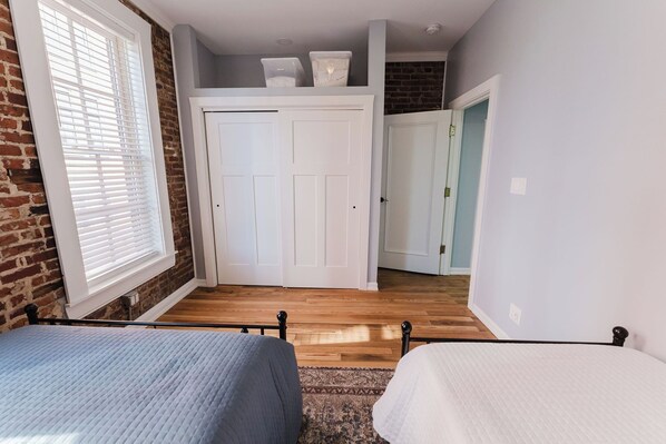 A bedroom with two beds, a brick wall, a white door, and a wooden floor. - Walk to Arch, Stadium & Dome! 2BR/2BA Downtown Gem ready for you and your family (St. Louis)