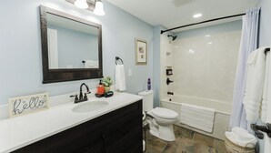 A bathroom with a white sink, black vanity, a large mirror, a toilet, a shower with a glass door, and a towel rack. - Walk to Arch, Stadium & Dome! 2BR/2BA Downtown Gem ready for you and your family (St. Louis)