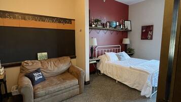 A hotel room with a sofa, a bed, a desk, and a wall with alphabet letters.