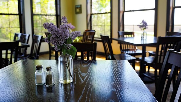 Un comedor con una mesa dispuesta para dos personas, con un jarrón de flores moradas y saleros y pimenteros.
