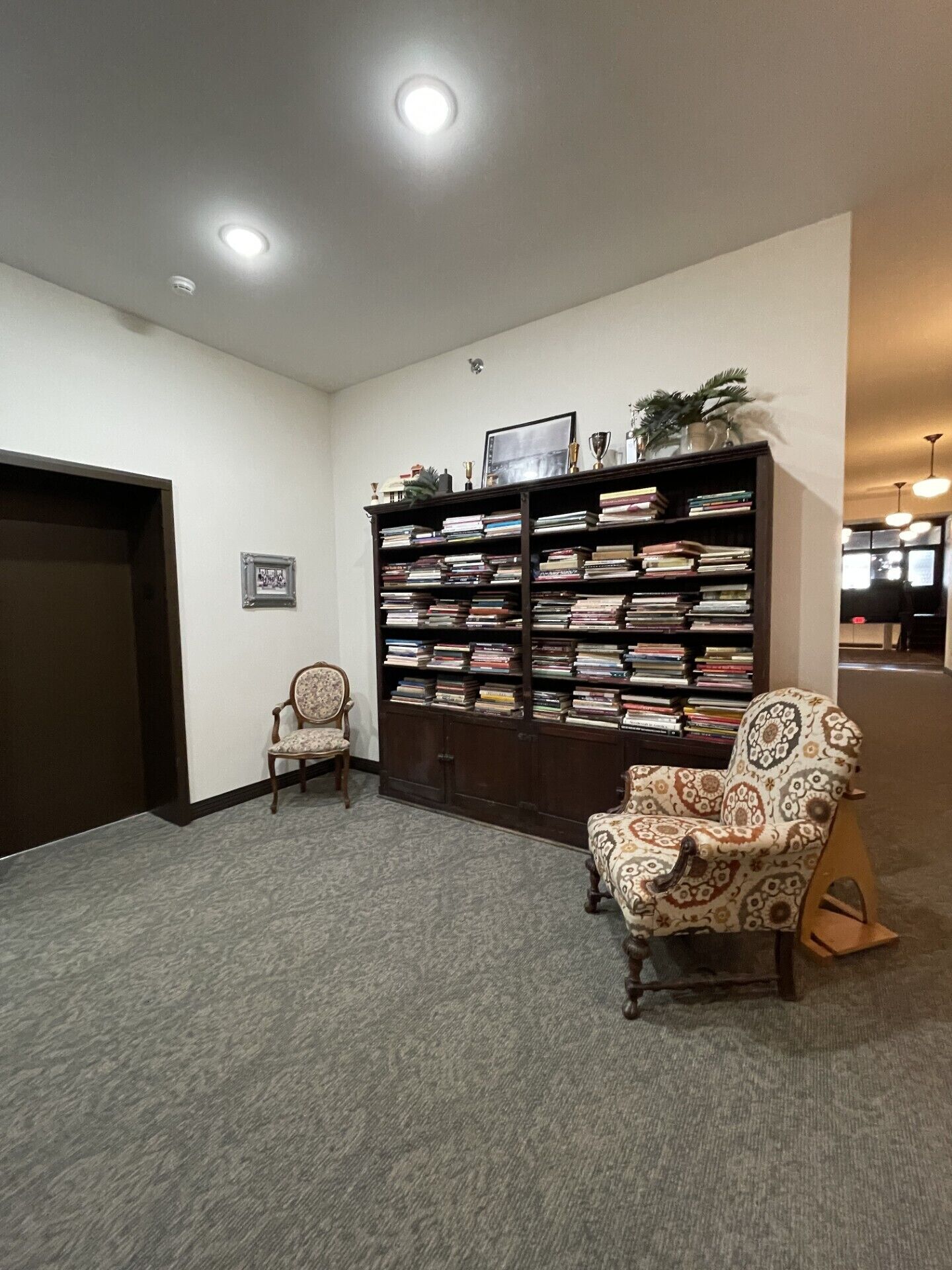 Una biblioteca con estanterías, dos sillones y una puerta.