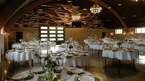 Un salón de banquetes con varias mesas redondas dispuestas para cenar, con manteles blancos, centros de mesa verdes y detalles dorados.