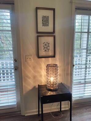 A room with a door, two framed abstract artworks on the wall, and a table with a glass candle holder. - Haile Village Condo, Beautiful Perfection. (Gainesville)
