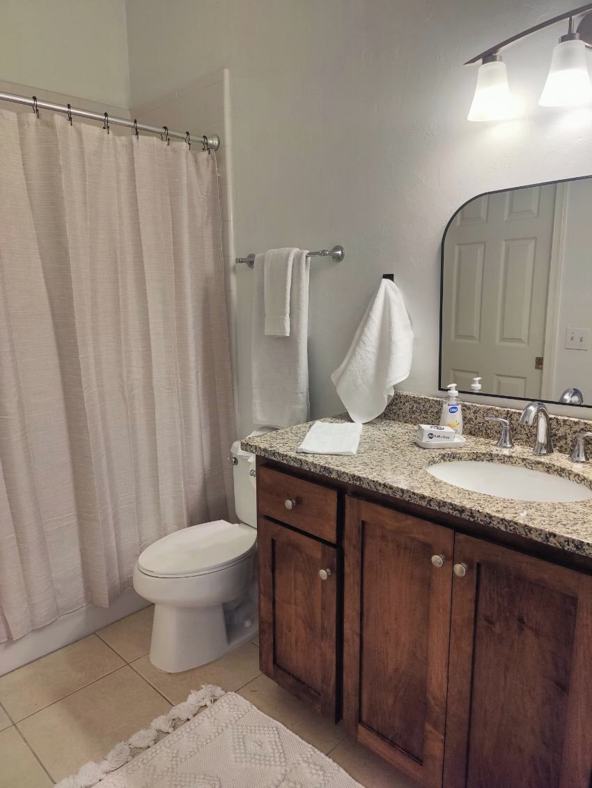 A bathroom with a shower curtain, a toilet, a sink with a mirror, and a towel rack.