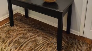 Una mesa de madera oscura con una cesta tejida que contiene frutas y una lámpara blanca.