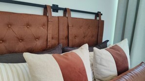 Una cama con cabecera capitonada, varios almohadones y un banco.