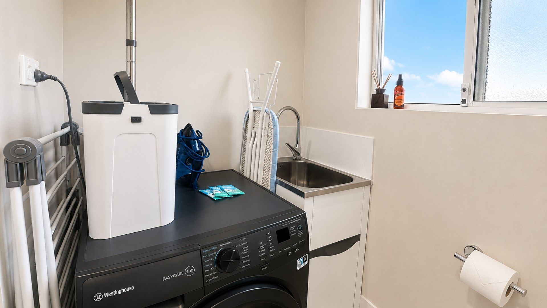 A compact laundry room with a washing machine, a drying rack, and a window with a view.