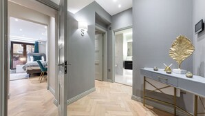 Un couloir moderne avec un parquet en chevrons, un mur gris orné d’un élément décoratif doré et une console dotée d’un cadre doré.