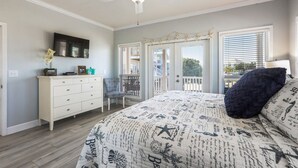 Un dormitorio con cama, cómoda, televisor y puertas al balcón.