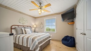 Un dormitorio con cama, ventilador de techo, televisor, ventana y puerta.