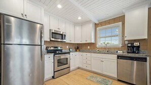 Una cocina moderna con armarios blancos, electrodomésticos de acero inoxidable, microondas, horno y lavavajillas.