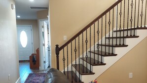 Una sala de estar con un sofá de cuero, un cojín colorido, un tapete estampado y una escalera con barandilla de madera.