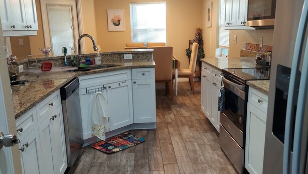 Una cocina moderna con armarios blancos, encimera de granito, electrodomésticos de acero inoxidable y suelo de madera.