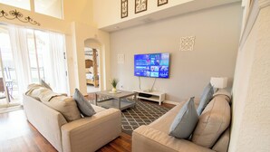 A living room with two beige sofas, a coffee table, and a flat-screen TV mounted on the wall. - Stunning 6 bedroom vacation villa (Kissimmee)