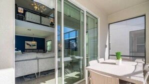 A modern apartment with a balcony, a dining area with wicker furniture, and a living room with a sofa and a painting. - Serene Rhyme Escape - Five Bedroom House, Sleeps 10 (Kissimmee)