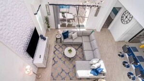 A modern living room with a sectional sofa, a coffee table, and a dining area with blue chairs. - Serene Rhyme Escape - Five Bedroom House, Sleeps 10 (Kissimmee)