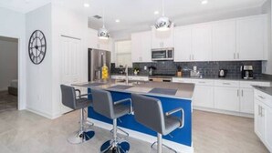 A modern kitchen with white cabinets, a blue island, and two bar stools. - Serene Rhyme Escape - Five Bedroom House, Sleeps 10 (Kissimmee)