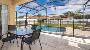 Um alpendre coberto com estrutura de vidro, piscina e mobiliário para área externa.