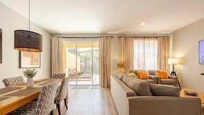 Ein modernes Wohnzimmer mit einer Couch, einem Esstisch mit Stühlen und einem großen Fenster mit Vorhängen.