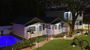 Una casa de dos pisos con piscina, un patio cubierto y un jardín bien iluminado.