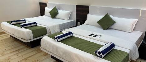 Ett hotellrum med två sängar, var och en med ett grönt och vitt överkast, vita kuddar och prydligt hopvikta handdukar.