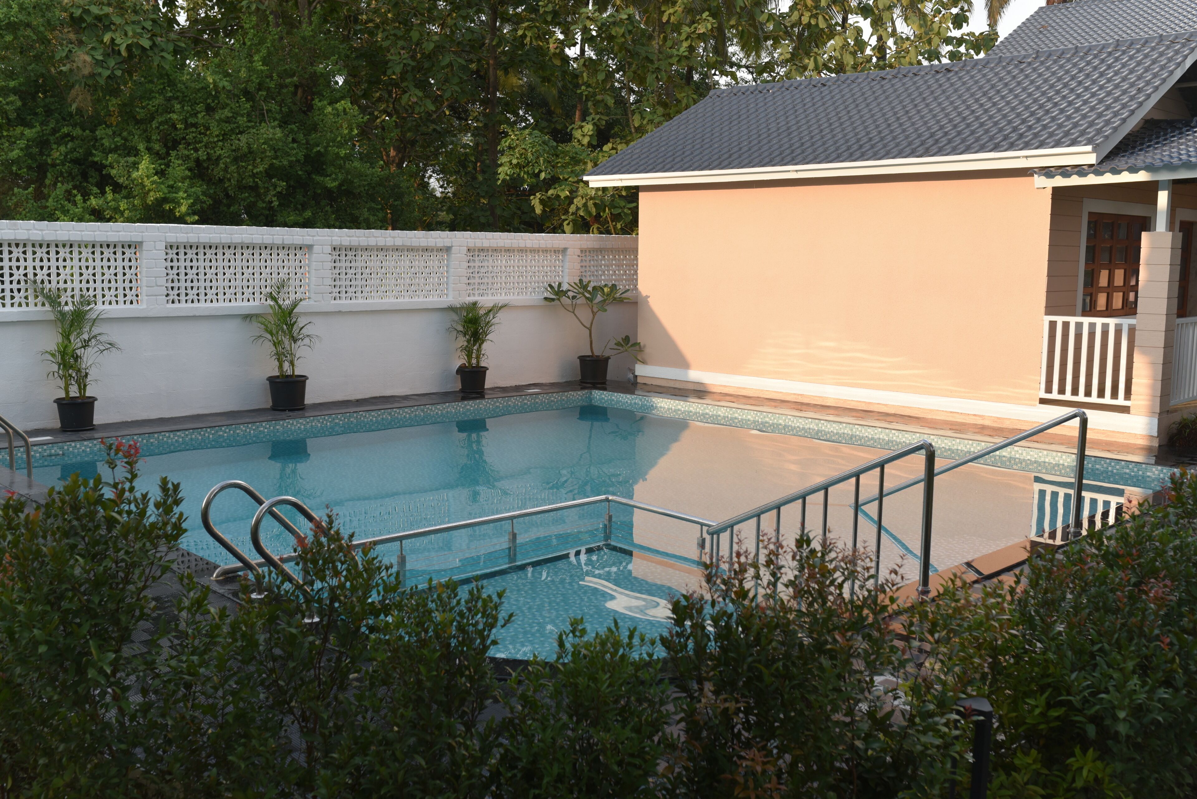 A swimming pool with a white fence, potted plants, and a building with a tiled roof.