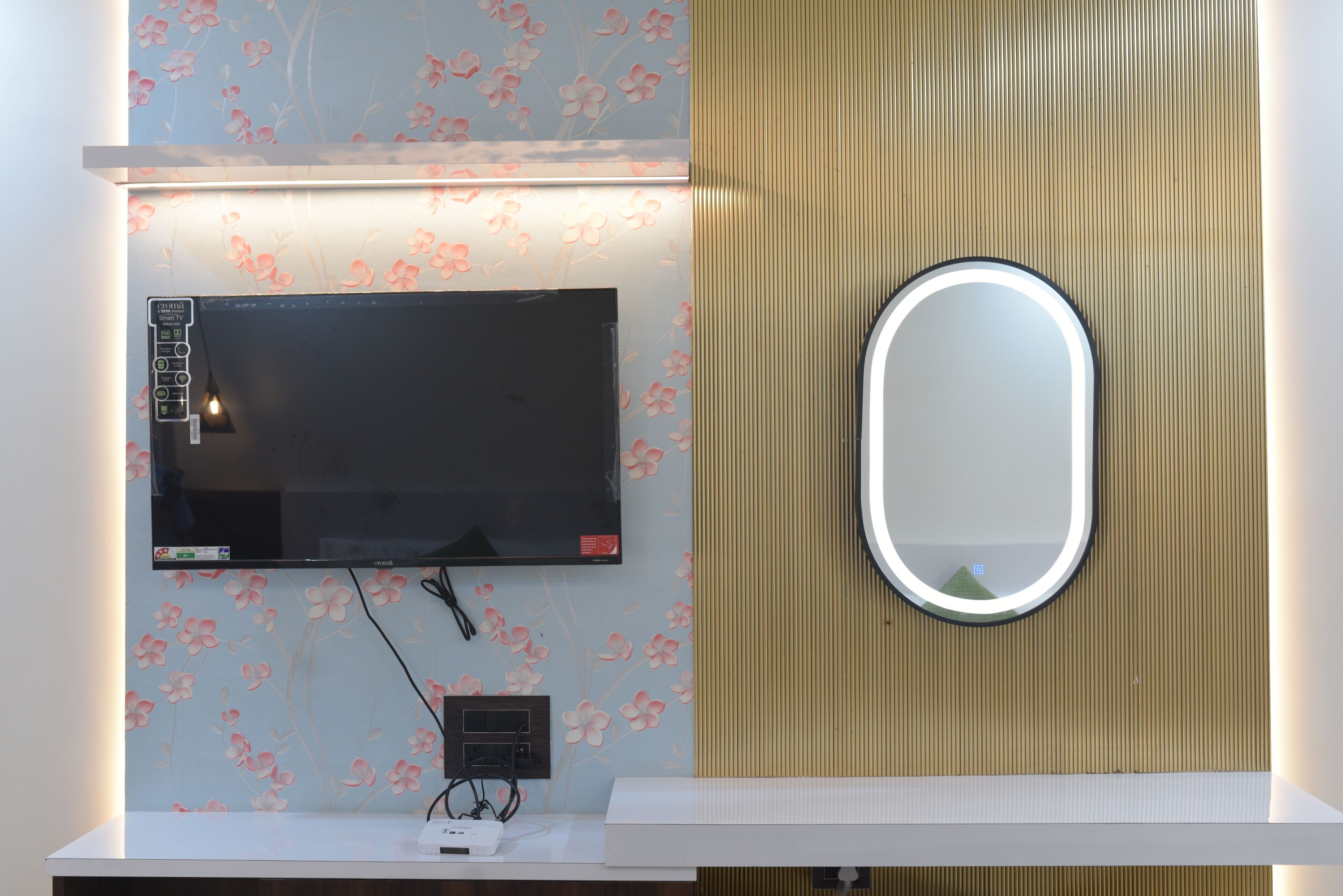 Un baño con televisor montado, un espejo y un tocador blanco.