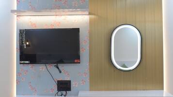 Un baño con televisor montado, un espejo y un tocador blanco.