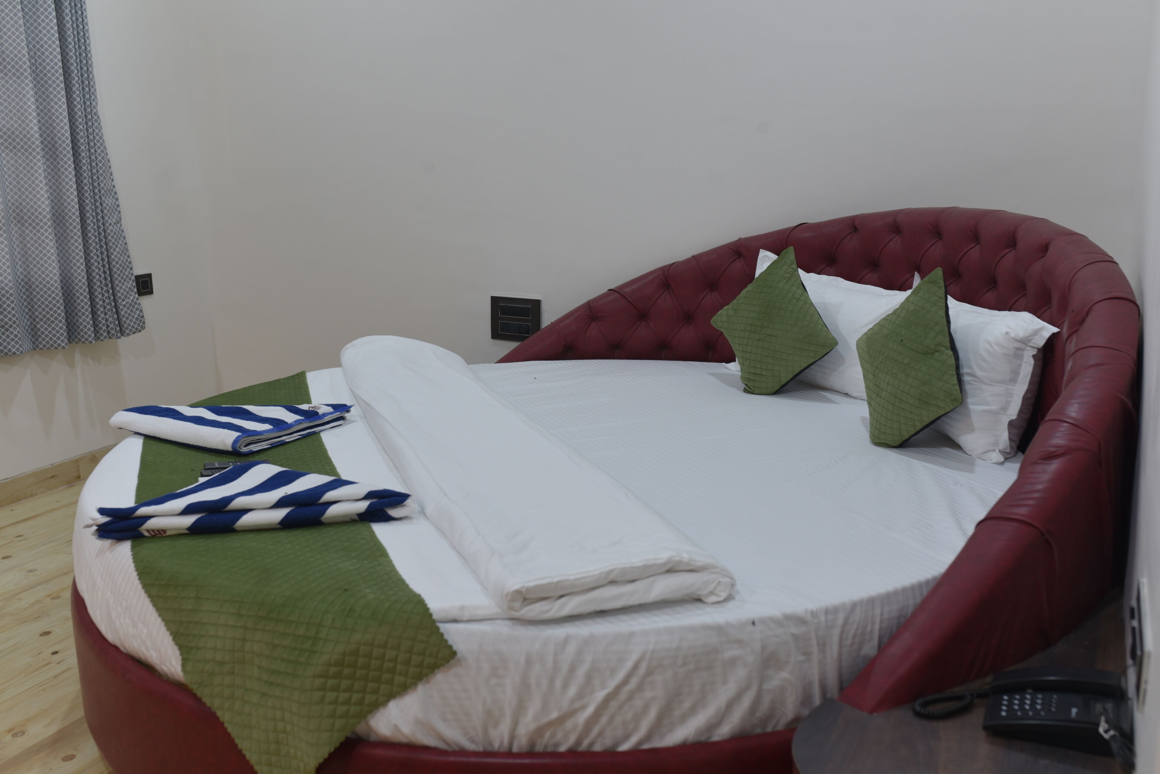 A neatly made bed with a red headboard, white bedding, and green and white pillows.