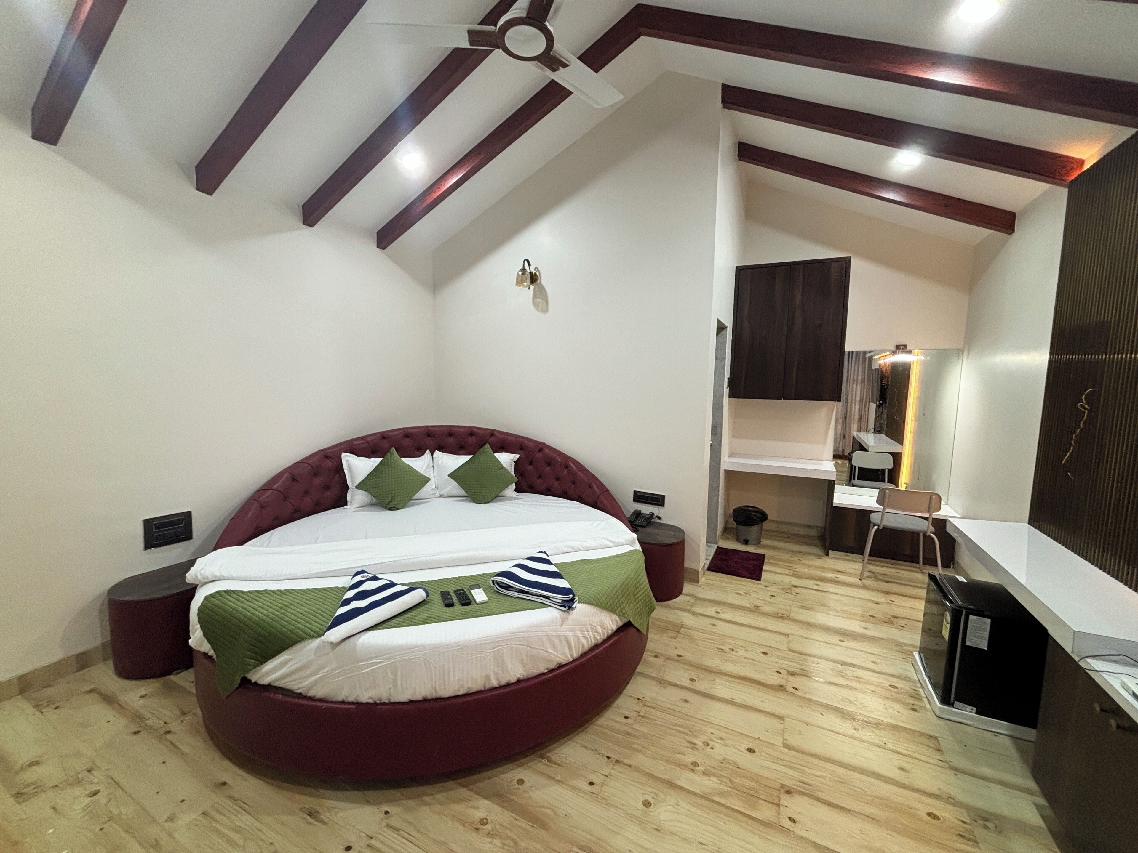 A bedroom with a curved bed, wooden flooring, a ceiling fan, and a desk area with a chair.