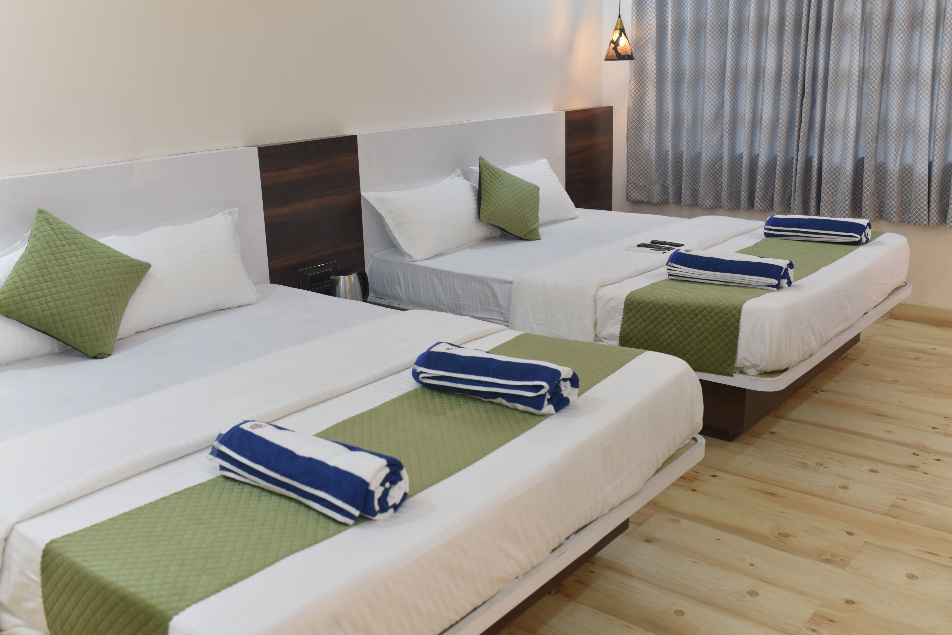 A hotel room with three single beds, each with a green and white bedspread and matching pillows.