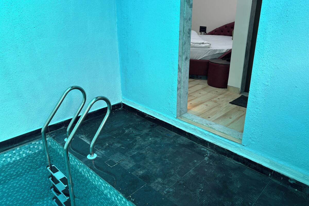 Ein Schwimmbecken mit Metallleitern, einem gefliesten Boden und einem Holzboden im angrenzenden Raum.