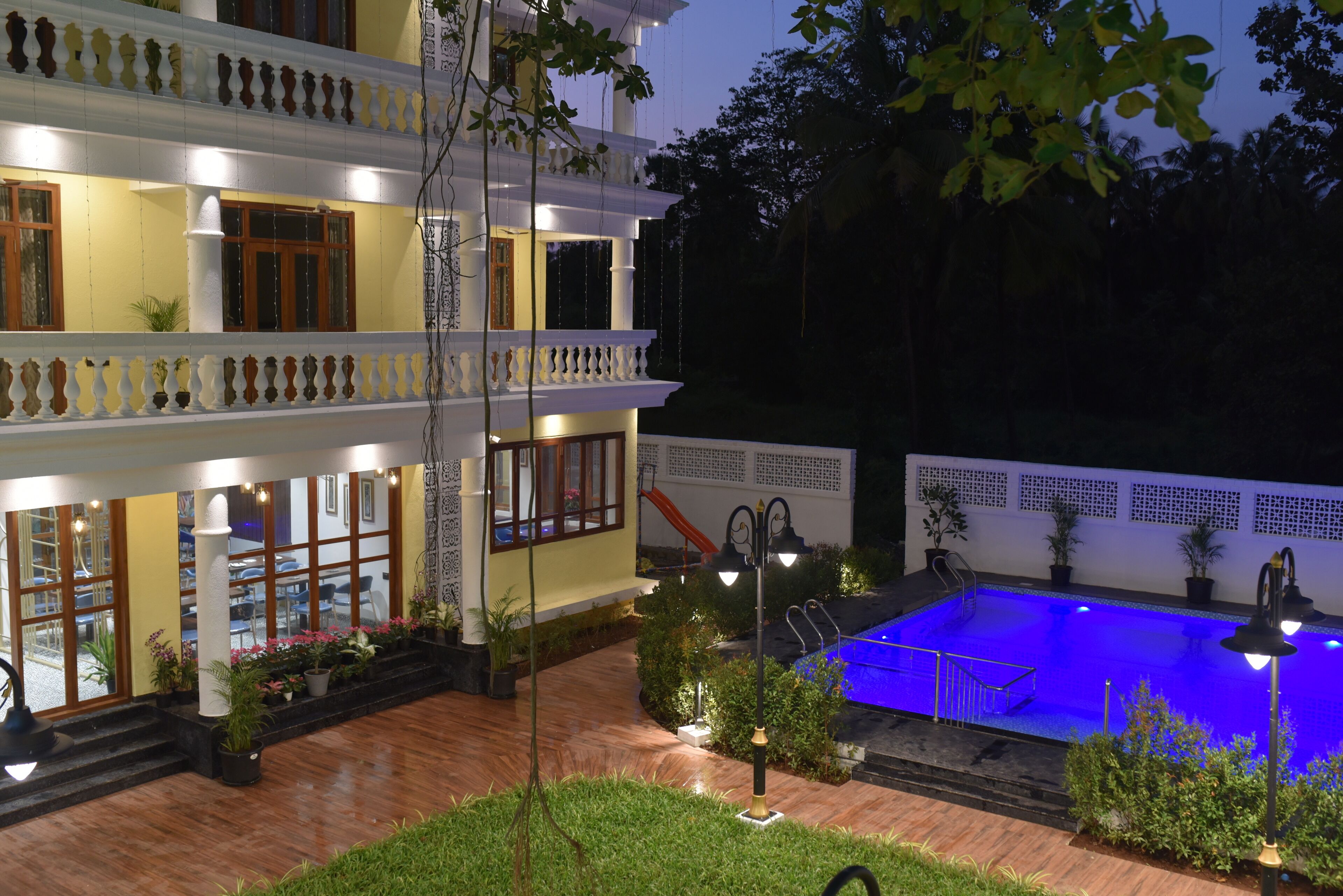A two-story building with a swimming pool, outdoor lighting, and potted plants.