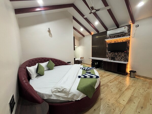 A bedroom with a curved bed, a ceiling fan, an air conditioning unit, and a TV mounted on a wall. - ILIF 2706 Western Breeze Villas (Nagaon)