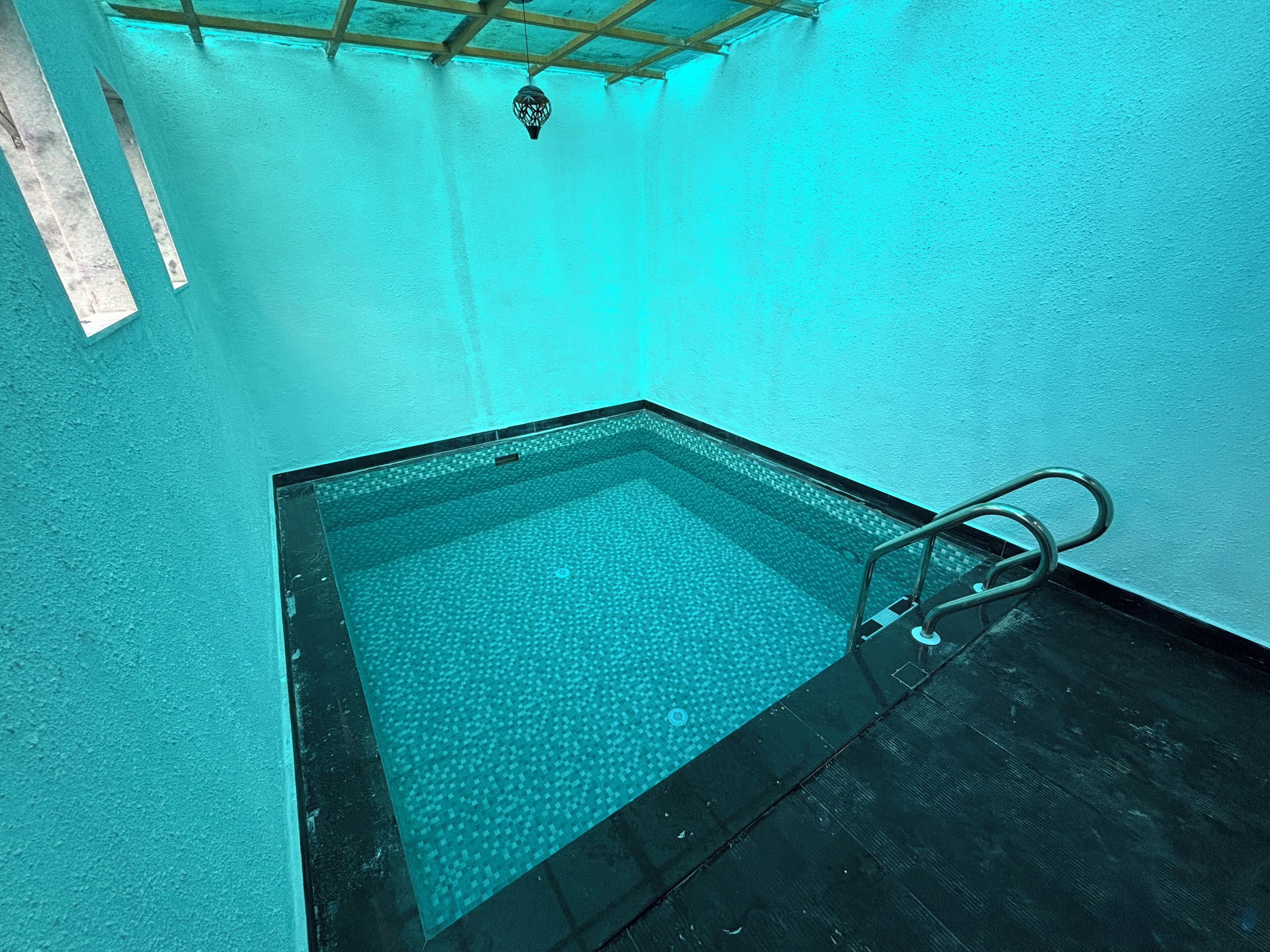 Un petit bain à remous rectangulaire, doté d’un sol carrelé et d’une échelle en métal.